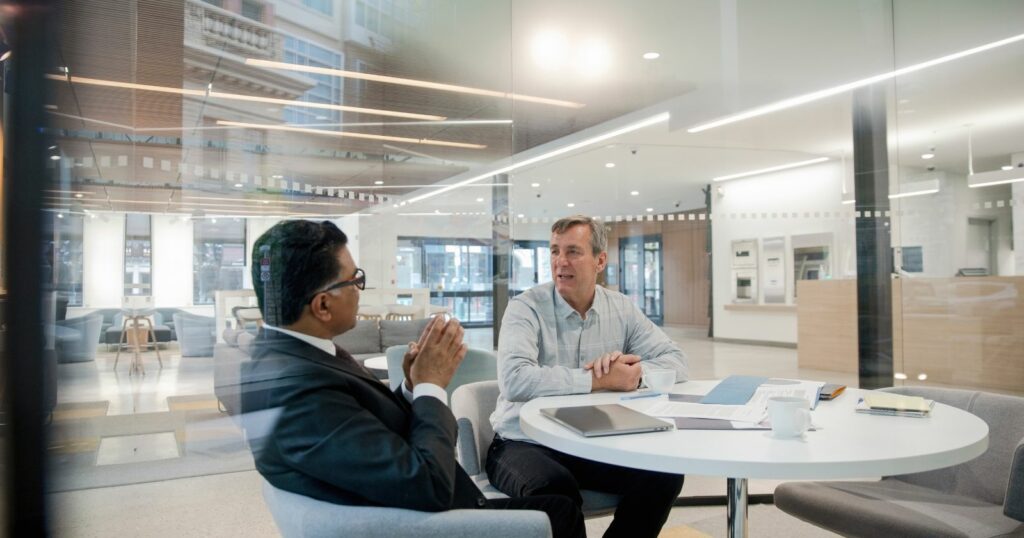 Two men sitting at a table in an office, discussing matters with creditors.