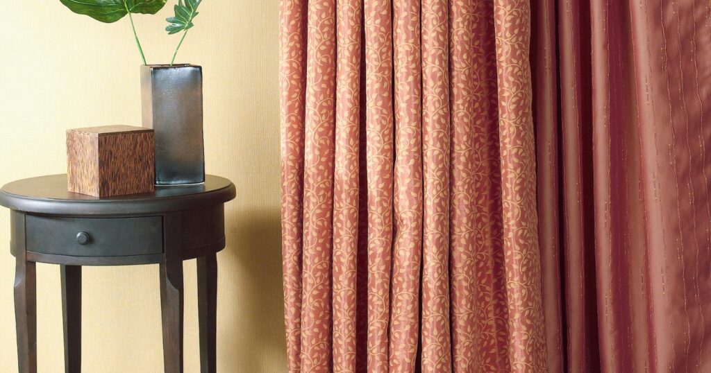 Decorative vase with plant on side table near pinstriped window valance.