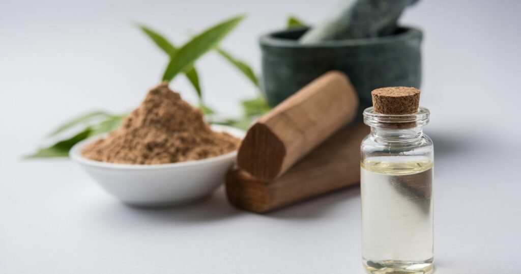 Cinnamon oil and wooden bowl with mortar and pestle, with sandalwood oil nearby.