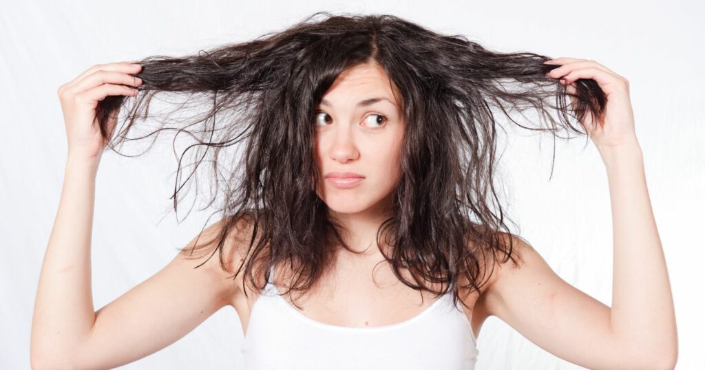 Woman with dry, long hair holding her head up.