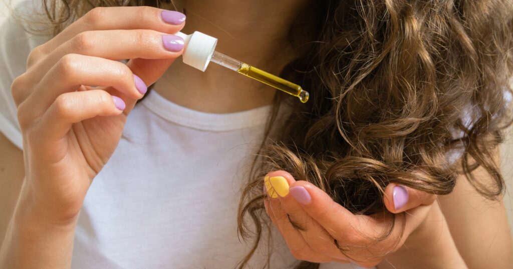 Woman holding hair oil bottle for curly hair care.
