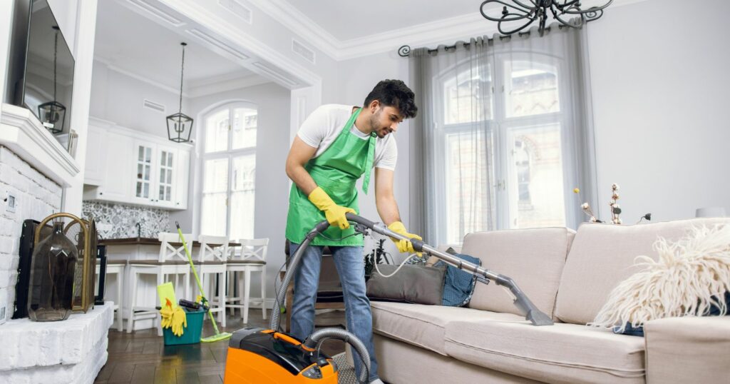 A man in an apron meticulously cleans a couch, showcasing modern furniture maintenance.