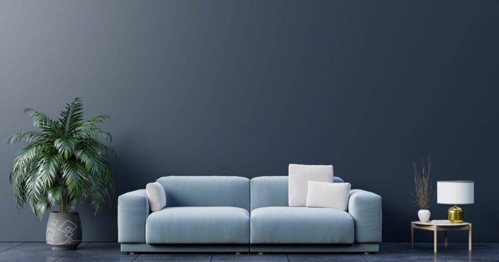 A modern blue sofa and a plant placed in front of a dark wall.