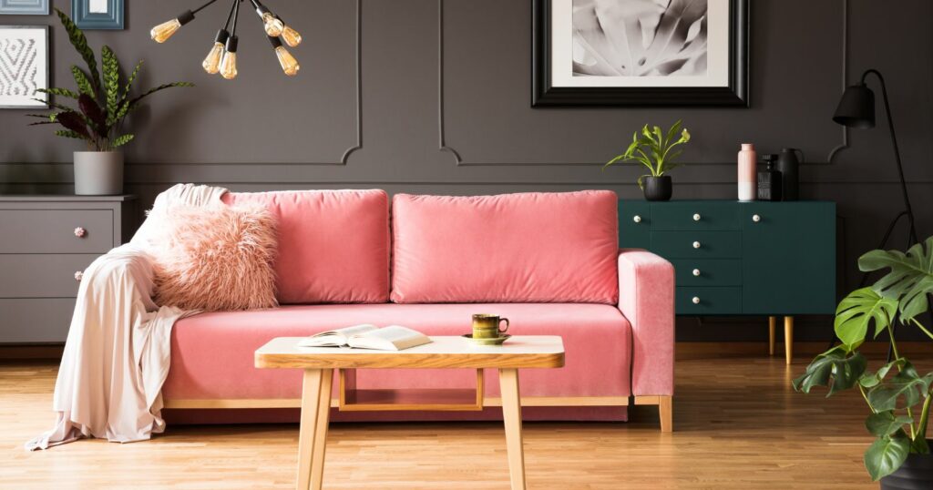 Modern pink couch in a room with wooden table and plant.