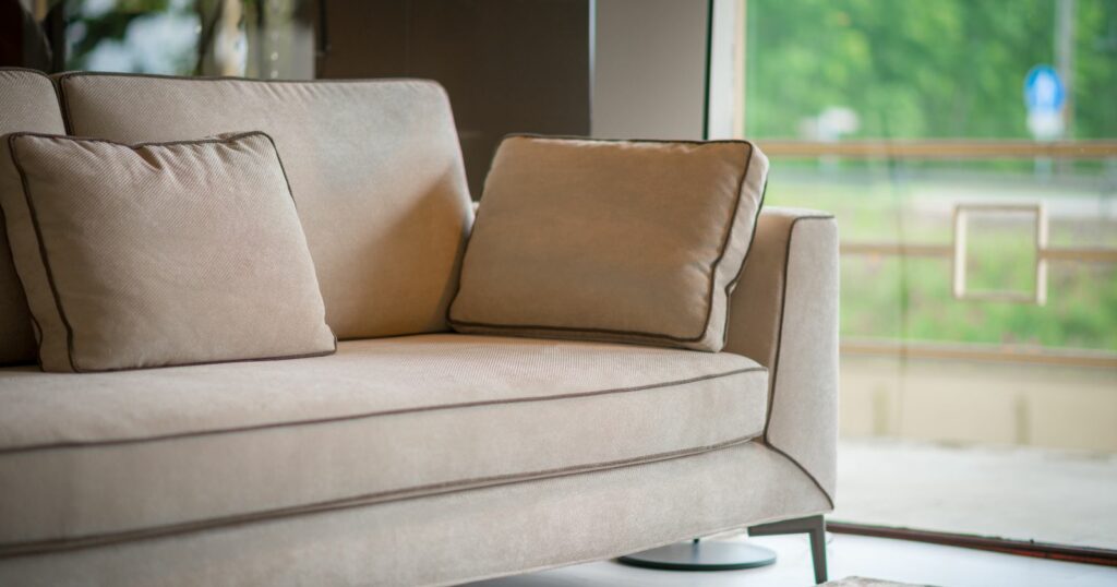 A modern sofa with two pillows placed in front of a window, showcasing its durability and high-quality materials.