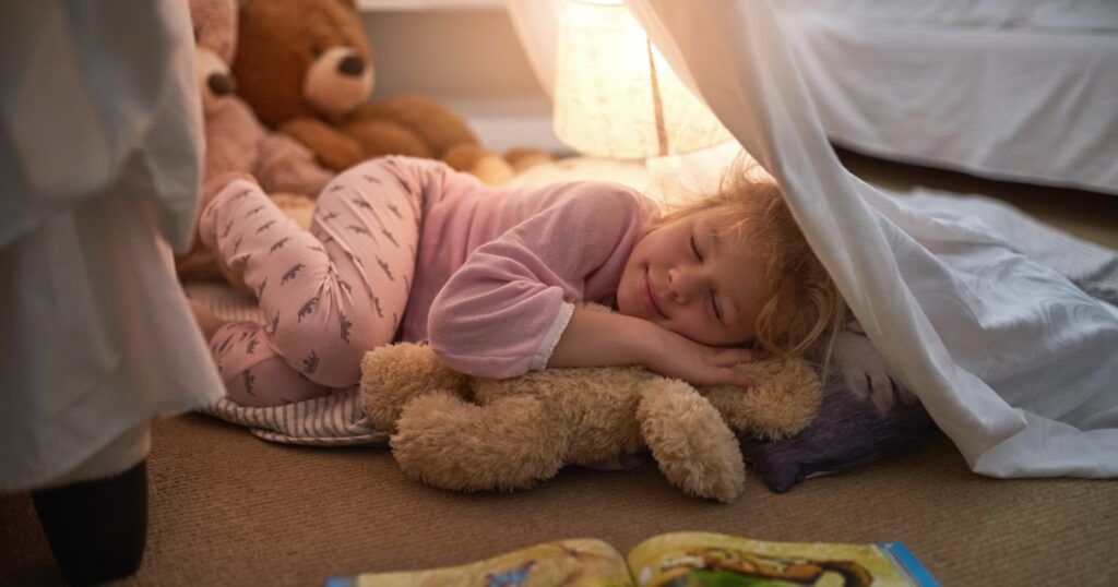 A peaceful slumber: a little girl cozily rests under a blanket, accompanied by her beloved teddy bear. Good night sleep.