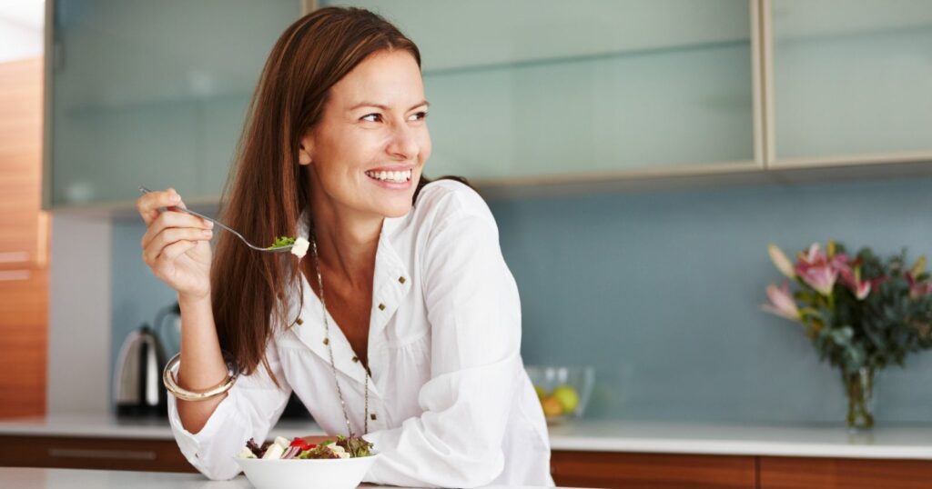 A woman happily enjoys a salad, radiating joy with her smile. The image depicts a healthy meal choice.