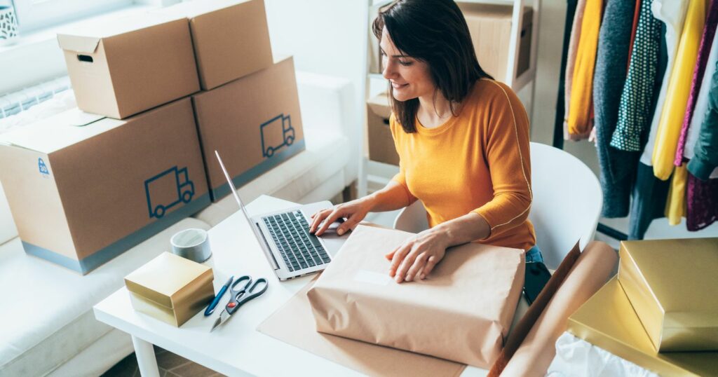 A woman at a table with boxes and a laptop, using tools for small business owner.