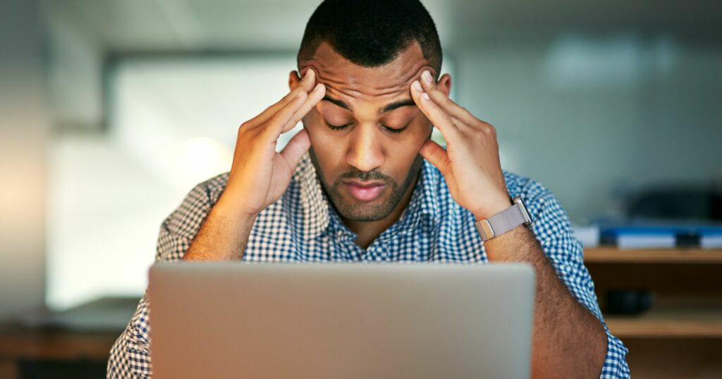  Stressed man at desk with head in hands.