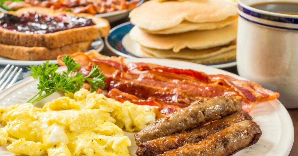 A hearty breakfast spread featuring sausage, bacon, eggs, toast, and a steaming cup of coffee.