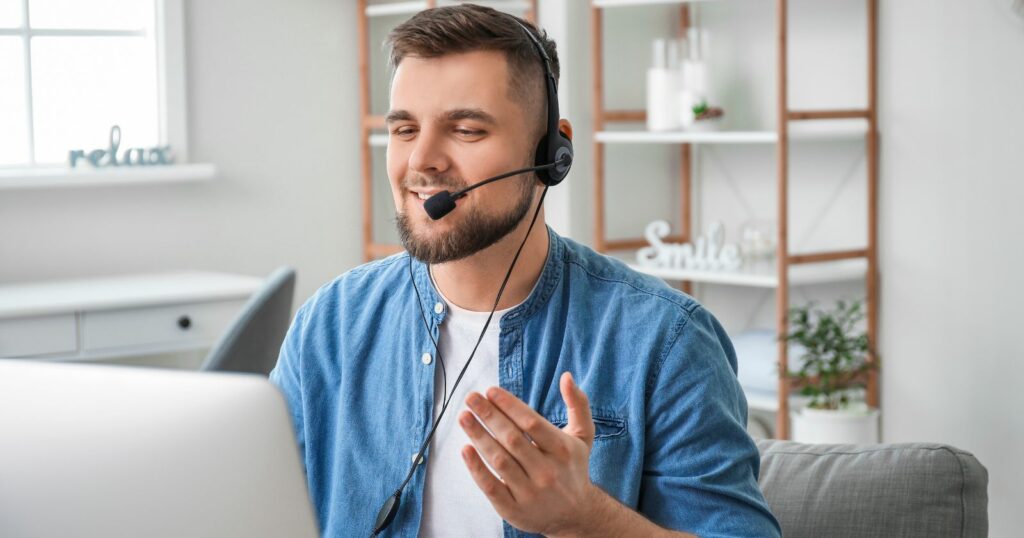 A man in a call center, wearing a headset, sits in front of a laptop, ready to assist customers.