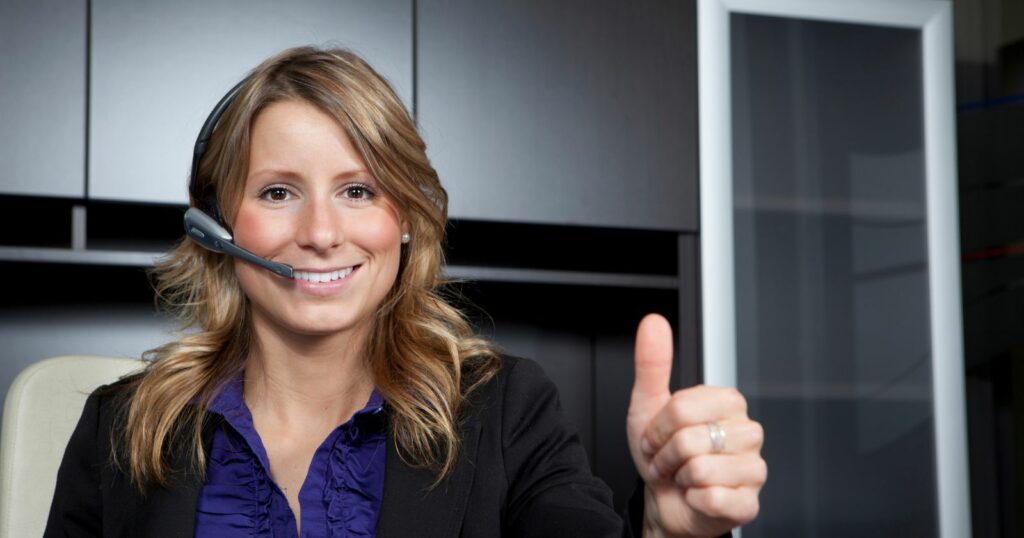 A woman in a call center wearing a headset and showing approval with a thumbs up gesture.