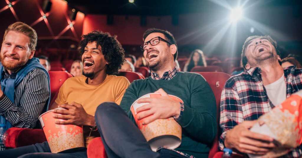 Three men enjoying a movie together in a theater, laughing and having a good time.