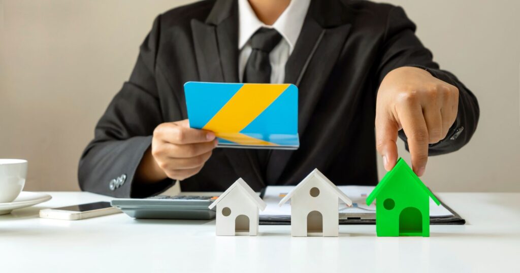 A man in a suit holds a credit card and a house model. Illustrating the topic of 'Current Trends in Home Equity Loan Rates'.