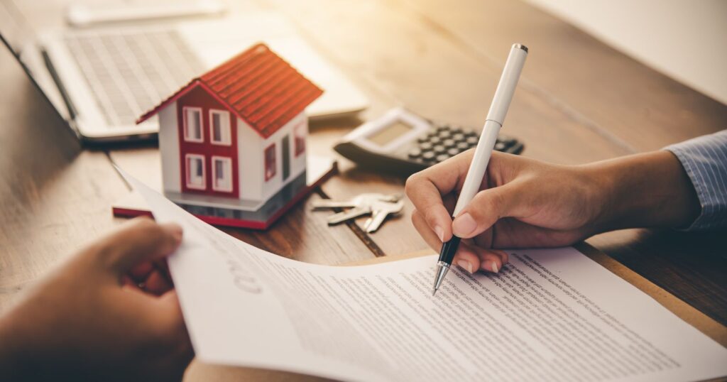 A man signs a contract with a house model on the table, symbolizing making an informed decision.