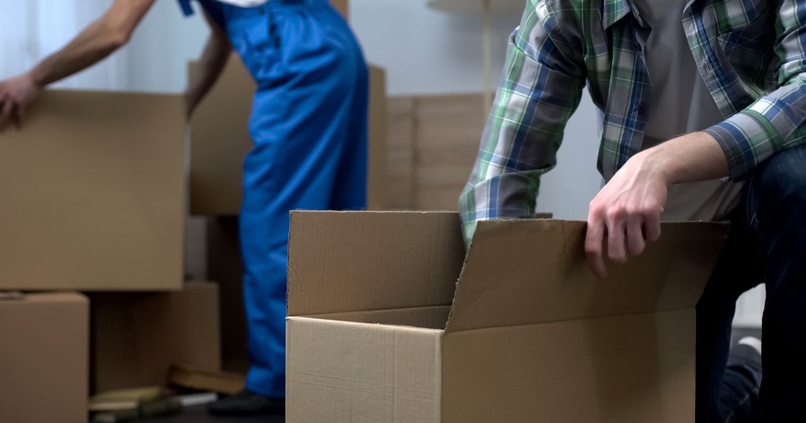 Two men from a Moving and Storage Company are carrying boxes into a room.