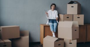 A woman sitting on a table surrounded by boxes, representing the challenges faced by residential moving companies in enhancing their online strategy in 2024.