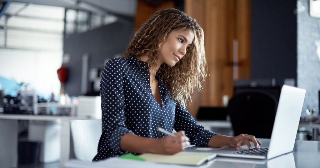 A woman sitting at a desk with a laptop, engaged in market research to stay ahead in the industry.