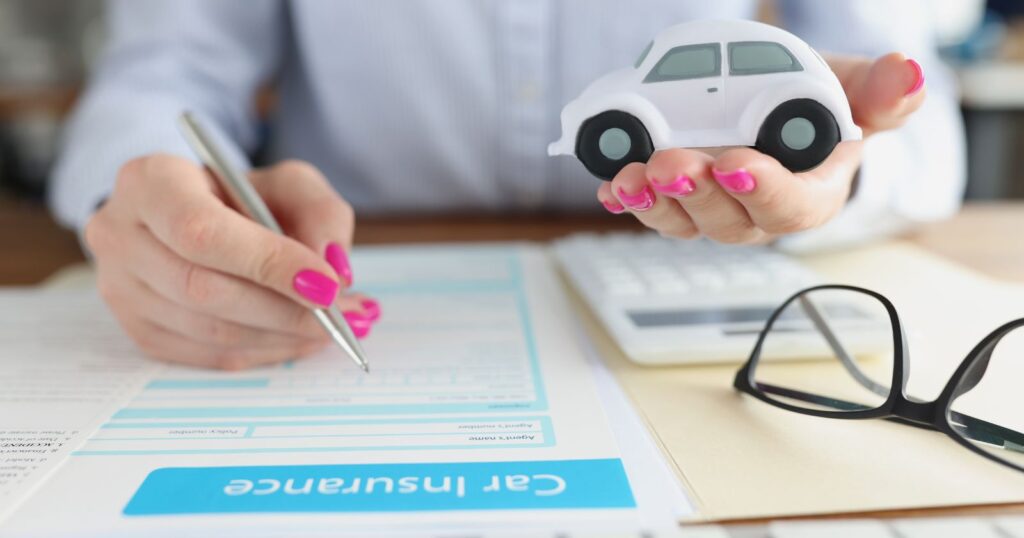 Woman holding car model on desk with pen and glasses, symbolizing car insurance.