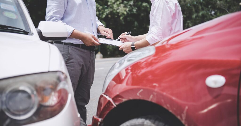 Two men standing next to a car holding a piece of paper. Components of Full Coverage Car Insurance.