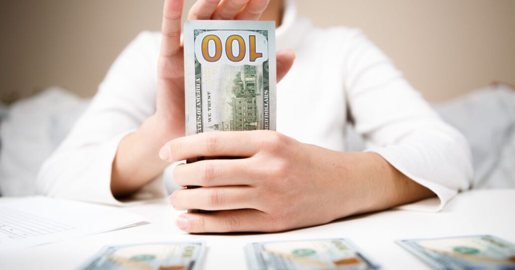 A person holding up a $100 bill. Image representing recommended tipping ranges.