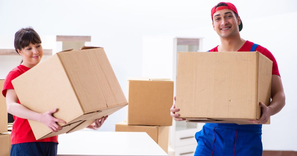 Two movers holding boxes in a room, illustrating the impact of tipping on their work.