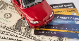 A small car perched on stacks of coins, symbolizing the cost of car insurance.