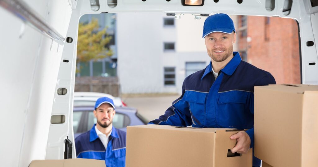 Two movers in blue uniforms carrying boxes, demonstrating the basics of tipping movers.