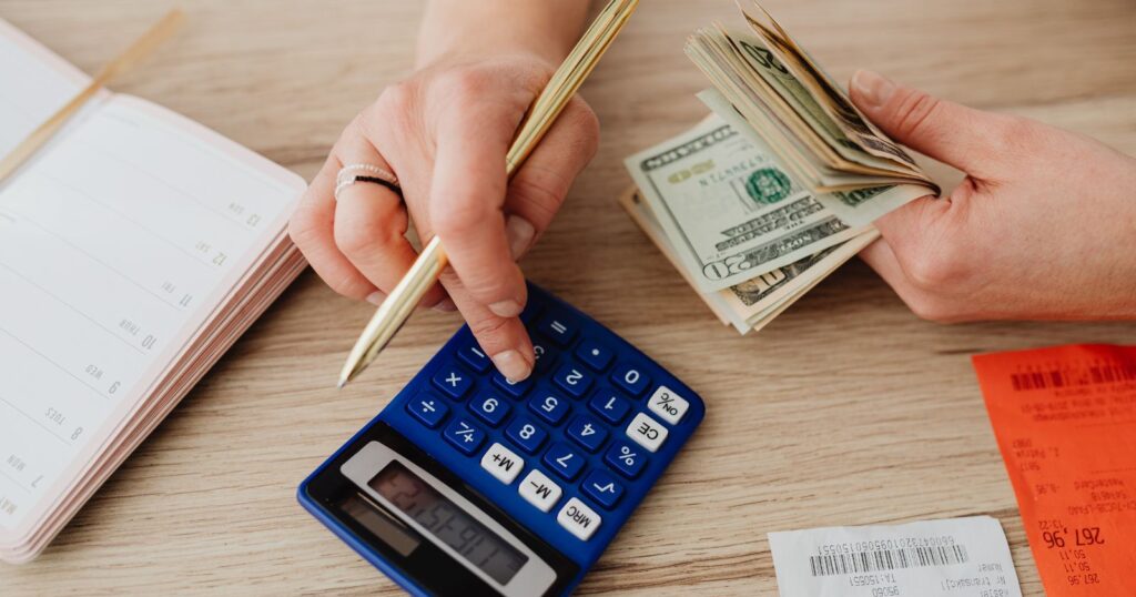 A woman's hand counting money on a calculator and notebook, demonstrating the process of calculating tips.