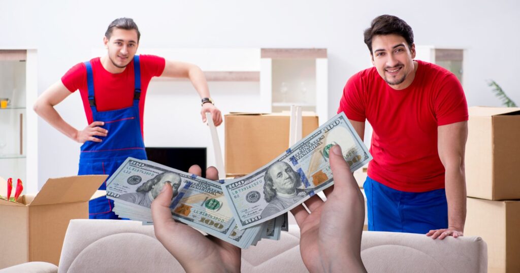 Two men holding money in front of moving boxes, symbolizing tipping etiquette during a move.