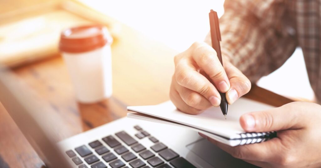 A person studying for the GED test with books, notebooks, and a laptop on a desk.